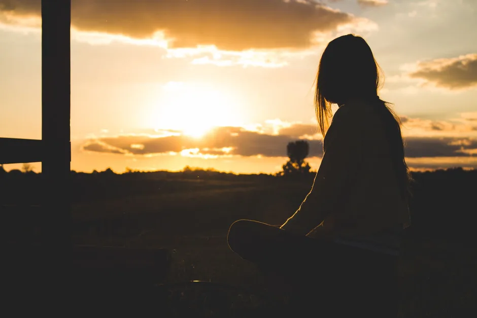 A person sitting quietly at sunset, taking a slow breath